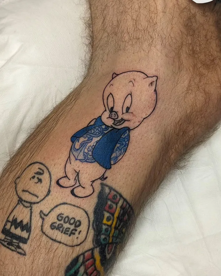 Colour Porky Pig tattoo next to a Charlie Brown tattoo on a leg
